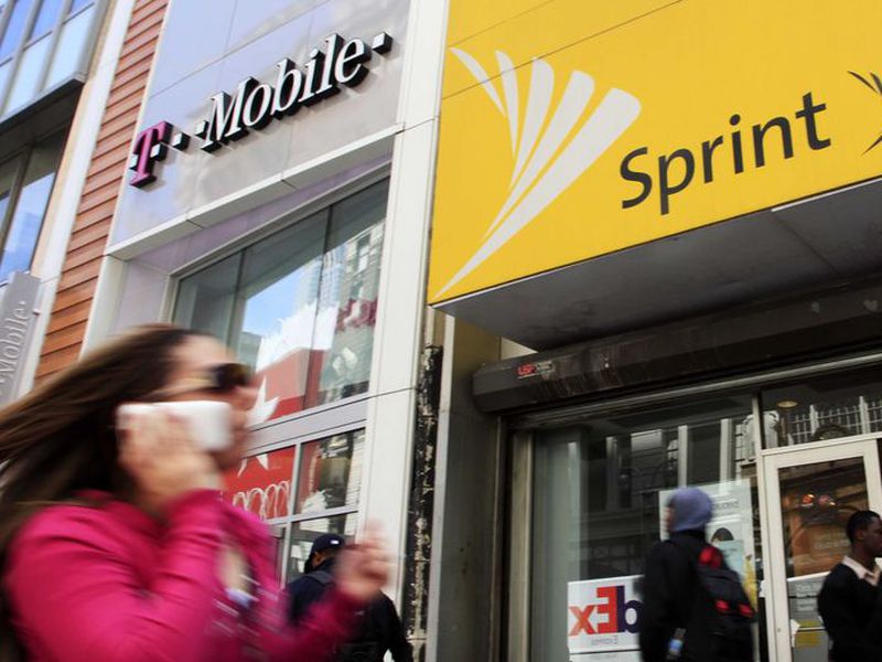 A woman using a cell phone walks past T-Mobile and Sprint stores in New
York. (AP)