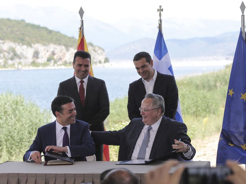 Greek Prime Minister Alexis Tsipras, background right, and his Macedonian counterpart Zoran Zaev, background left, look on as Greek Foreign Minister Nikos Kotzias, right, and his Macedonian counterpart Nikola Dimitrov sign an agreement on Macedonia’s new name in the village of Psarades, Greece