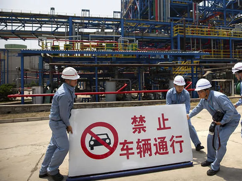 Workers move a sign near facilities for producing polypropylene at the Sinopec Yanshan Petrochemical Company on the outskirts of Beijing.