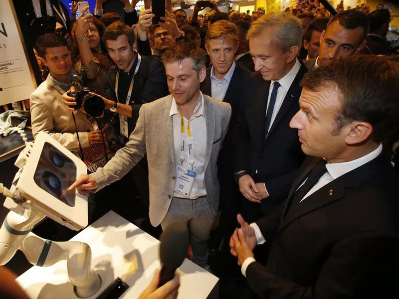 CEO of Spoon.ai Jerome Monceaux, left, points to a screen as he talks to LVMH luxury group CEO Bernard Arnault, center, and French President Emmanuel Macron as they visit the VivaTech gadget show in Paris.