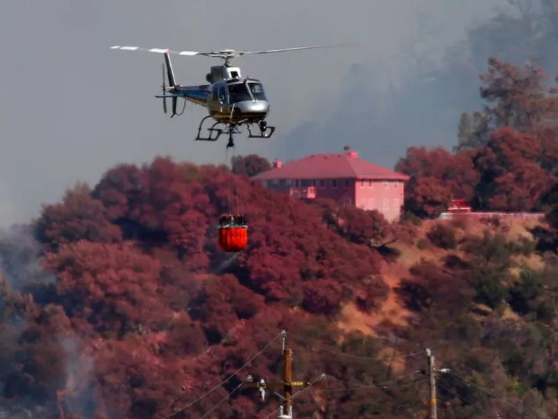 A helicopter battling a fire on Mt. Diablo passes a home covered in fire retardant,
Wednesday, July 25, 2018, above Marsh Creek Road east of Clayton,
Calif.