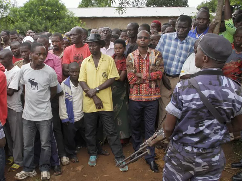Policemen stand guard as residents gather at the scene where more than 20 people were killed in their homes in an overnight attack in the Ruhagarika community of the rural northwestern province of Cibitoke. (AP)