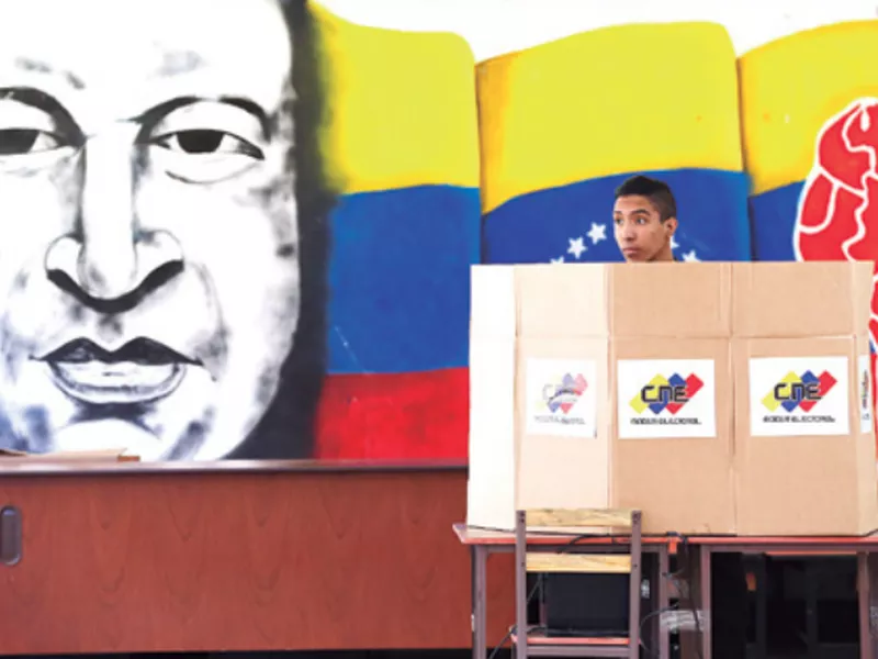 A voter chooses his candidate next to a mural of late Venezuelan President Hugo Chavez during presidential elections in Caracas, Venezuela. (AP)