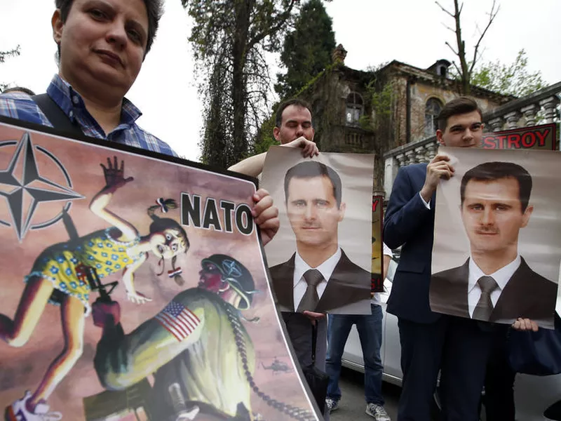 People hold pictures of Syrian President Bashar al-Assad and an anti NATO poster during a protest outside the Syrian embassy in Belgrade, Serbia, Sunday, April 15, 2018. A few dozen people took part in an anti-war rally opposing the military strikes by western countries in Syria. (AP Photo/Darko Vojinovic).