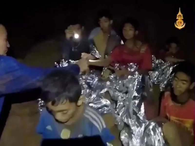 The 12 boys and their coach are seen in the video sitting with Thai navy SEALs in the dark cave.