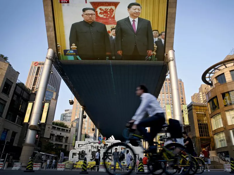 People bicycle past a giant TV screen broadcasting the meeting of North Korean leader Kim Jong Un and Chinese President Xi Jinping.