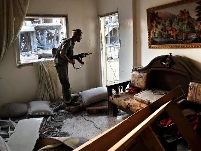 A U.S.-backed Syrian Democratic Forces fighter looks through a window from inside a destroyed apartment on the front line, in Raqqa, Syria.